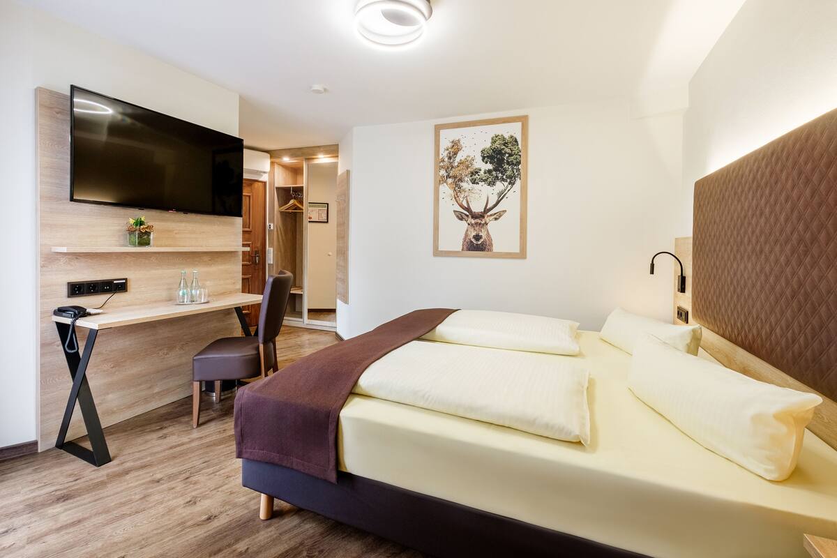 A modern hotel room with a bed, a desk, a chair, a TV, and a painting of a deer.