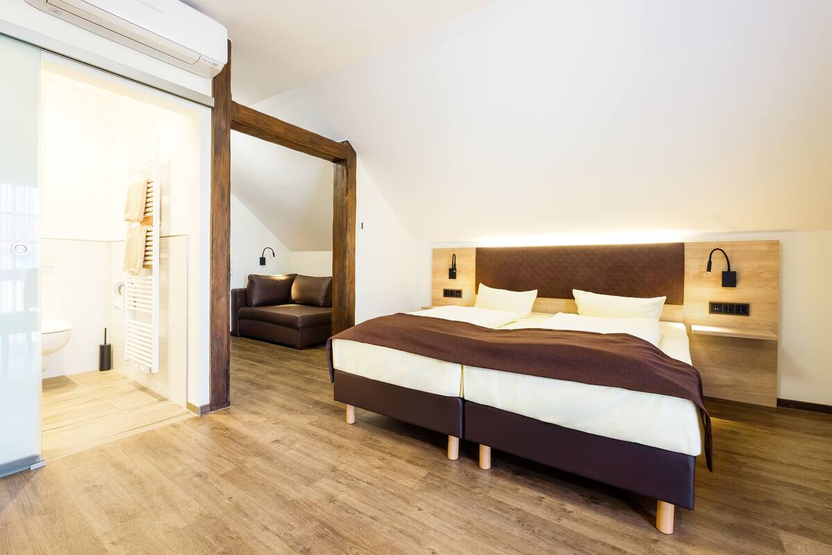 A modern bedroom with a large bed, wooden flooring, a built-in bench, and a wall-mounted light fixture.