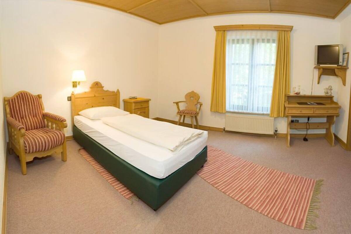 A hotel room with a bed, a chair, a desk, a television, and a window with curtains.