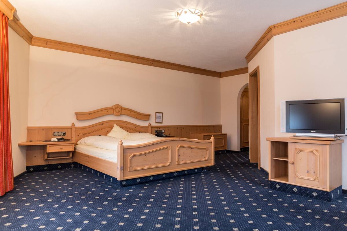 A hotel room with a wooden bed, a TV, a wooden cabinet, and a patterned carpet.