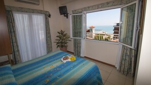 A room with a bed, a potted plant, a TV, and a balcony with a view of the sea. - Hotel Gabbiano (Porto San Giorgio)