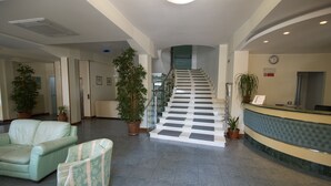 A hotel lobby with a reception desk, a staircase, and seating areas. - Hotel Gabbiano (Porto San Giorgio)