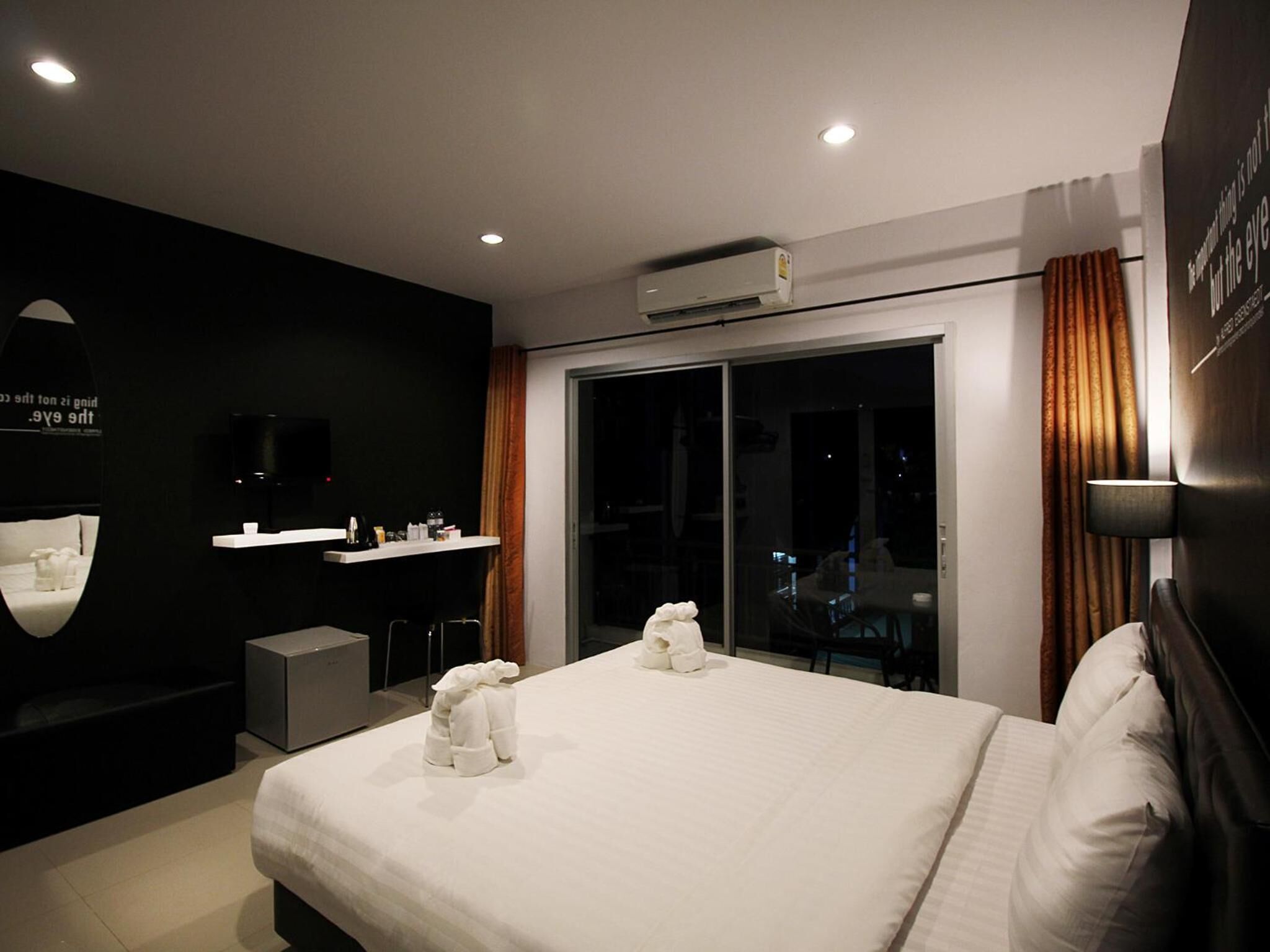 Ein modernes Hotelzimmer mit einem großen Bett, einem Flachbildfernseher, einer Minibar und Blick auf die beleuchtete Stadt bei Nacht.