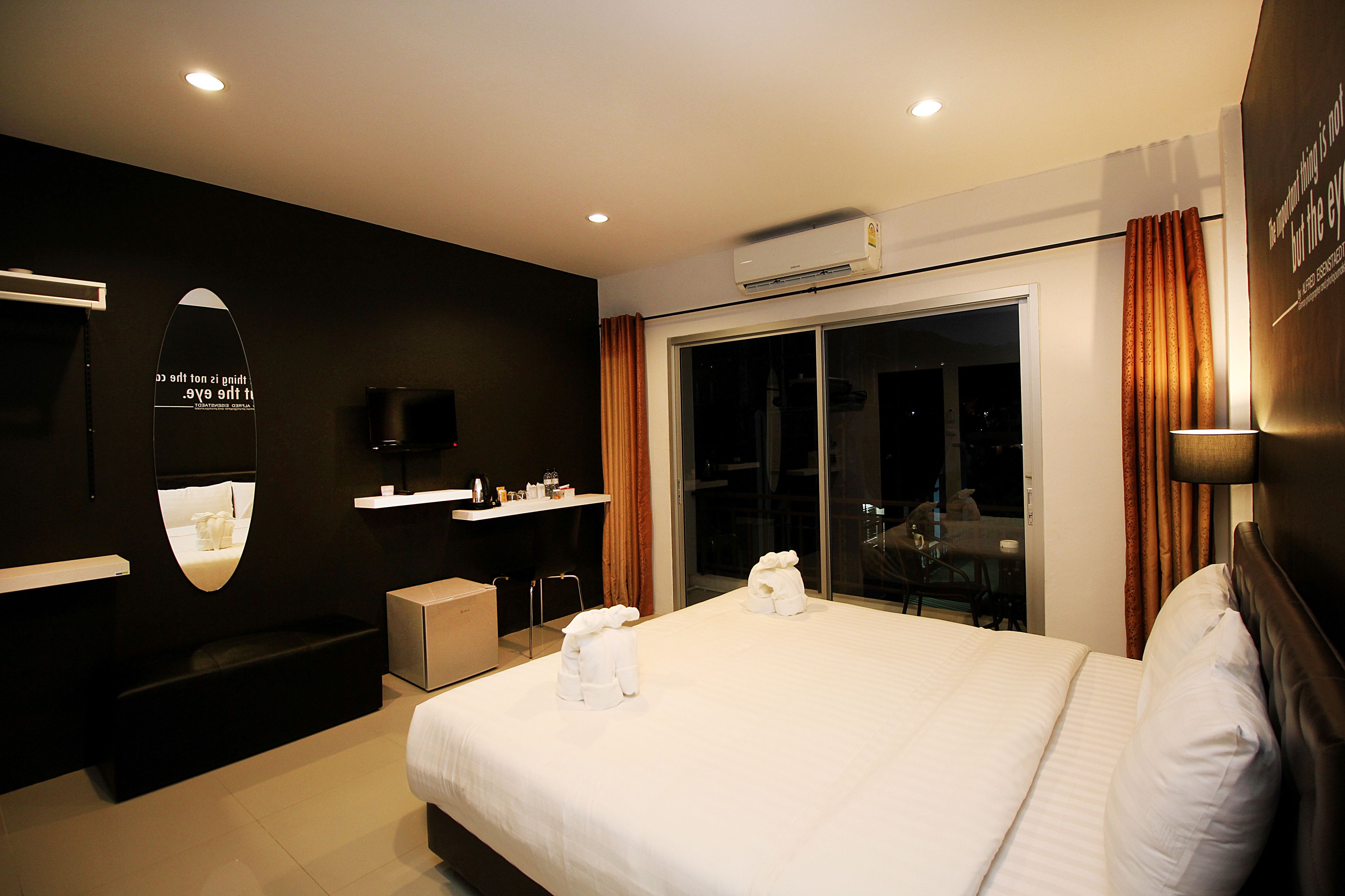 A modern hotel room with a large bed, a flat-screen TV, a built-in shelf, and a sliding glass door to the balcony.
