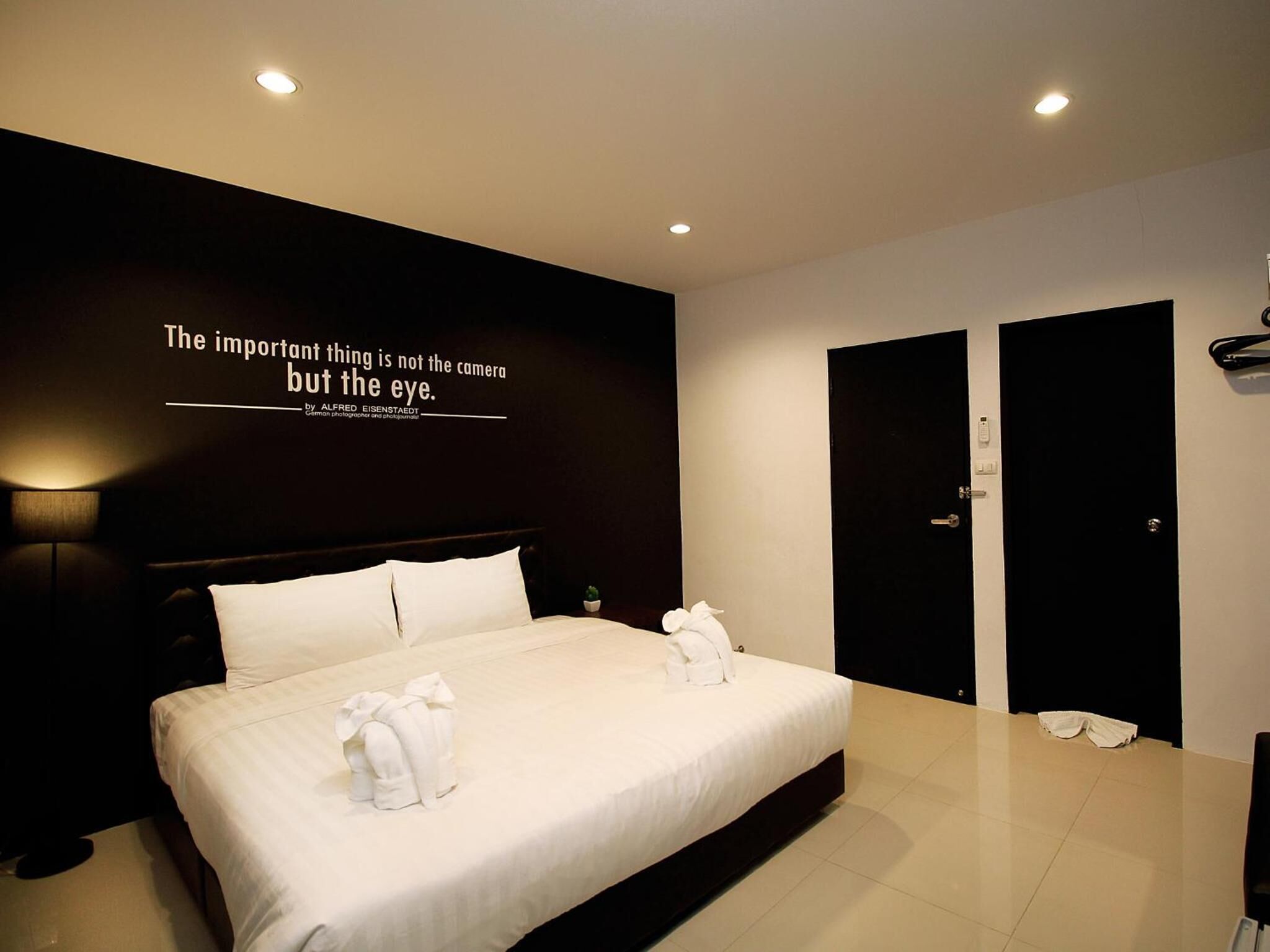 A modern hotel room with a large bed, a wall-mounted quote, and a pair of black doors.