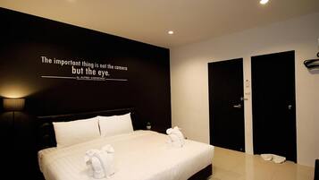 A modern hotel room with a large bed, a wall-mounted quote, and a pair of black doors.