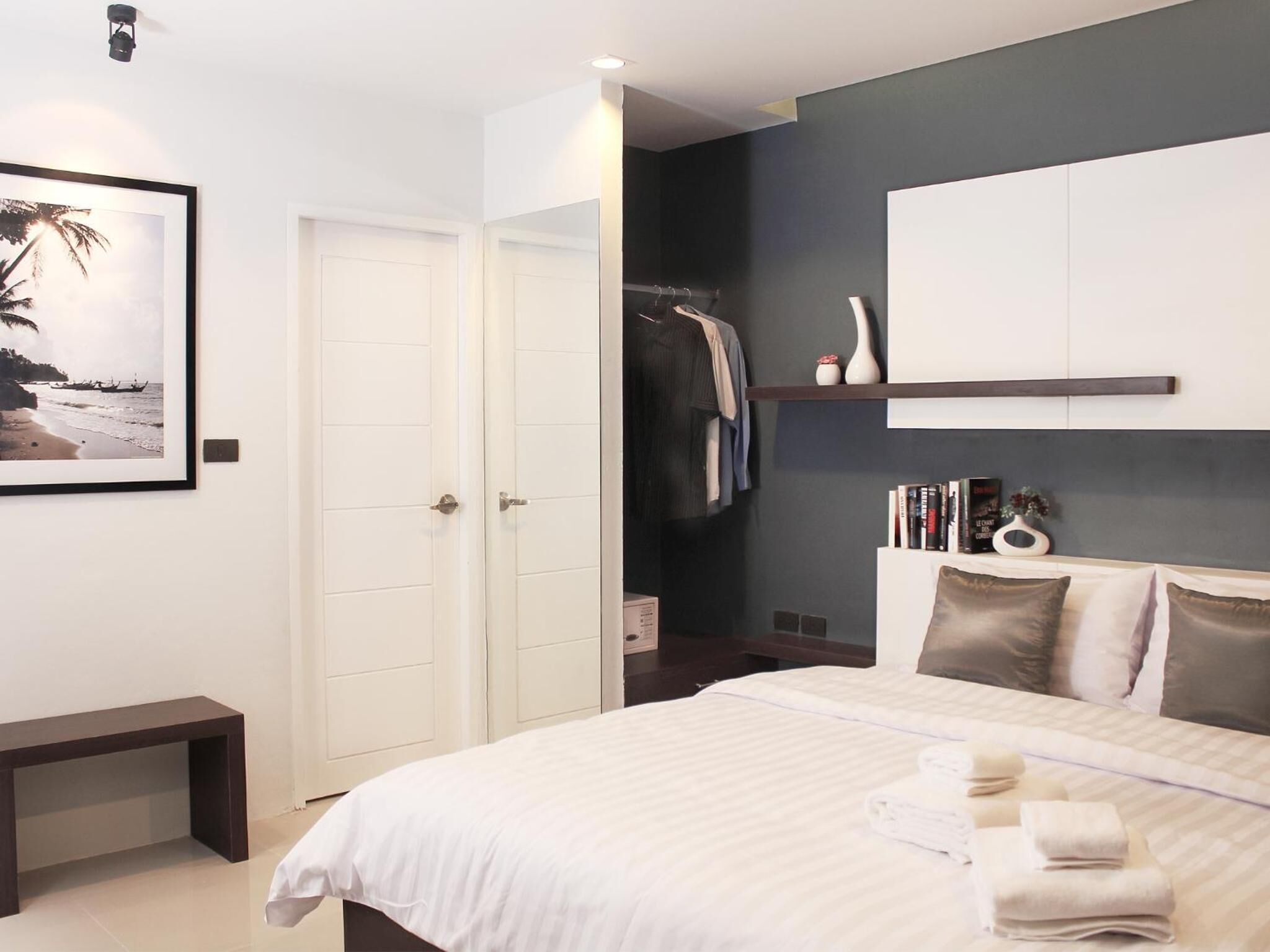 Une chambre d’hôtel comprenant un lit, un banc, une armoire et une étagère avec des livres et des objets décoratifs.
