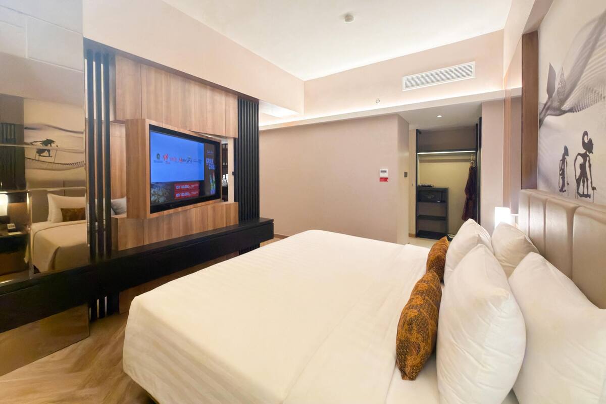 A hotel room with a large bed, a television, a mirror, and a painting on the wall.