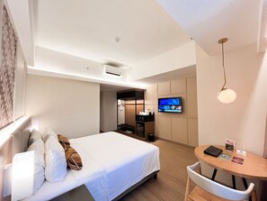 Ett hotellrum med en säng, ett skrivbord, en TV och en väggmonterad luftkonditioneringsanläggning.