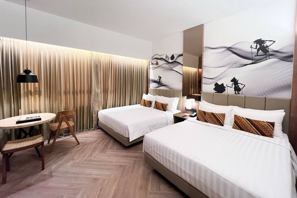 A hotel room with two beds, a desk, a chair, a lamp, and a large mirror.