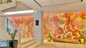 Een moderne lobby met een trap, een levendige muurschildering en potplanten.