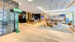 Een moderne hotellobby met een receptiebalie, een zithoek en een groot scherm dat content toont.