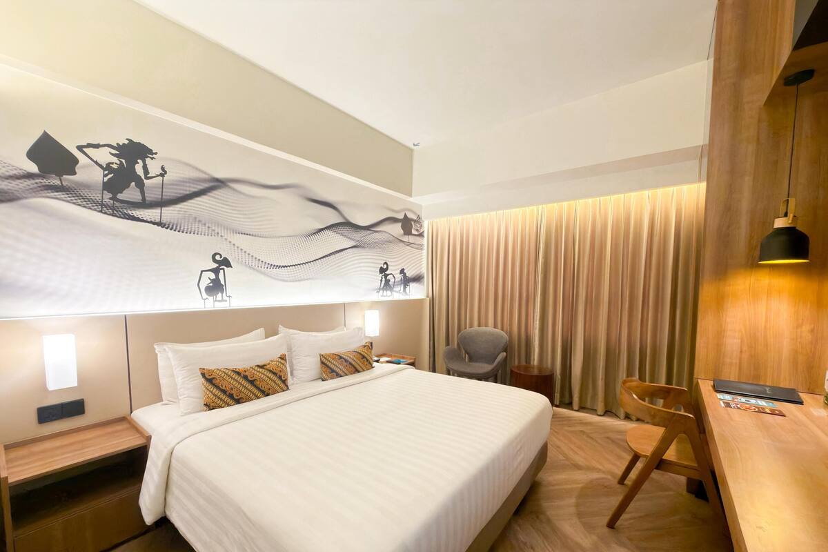 A modern hotel room with a large bed, a desk, a chair, and a wall with a decorative mural.