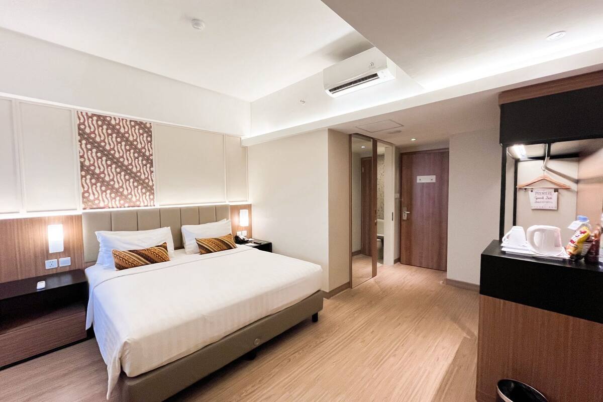 A hotel room with a bed, bedside tables, a mirror, a small kitchenette, and a door leading to a bathroom.