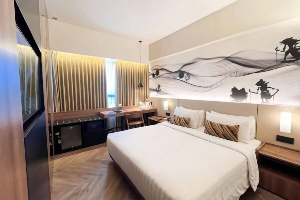A hotel room with a bed, desk, and a large wall mural.