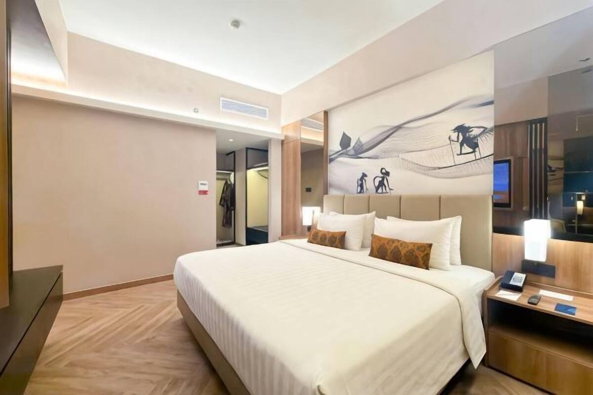 A hotel room with a large bed, a nightstand, a mirror, and a wall-mounted artwork.