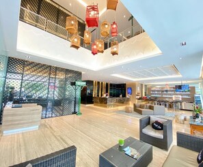 A modern hotel lobby with a reception desk, seating area, and a restaurant. - Grand Zuri Malioboro Yogyakarta (Yogyakarta)