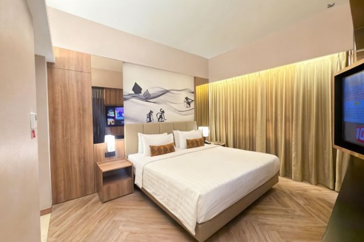 A hotel room with a large bed, a TV, a desk, and a wardrobe.