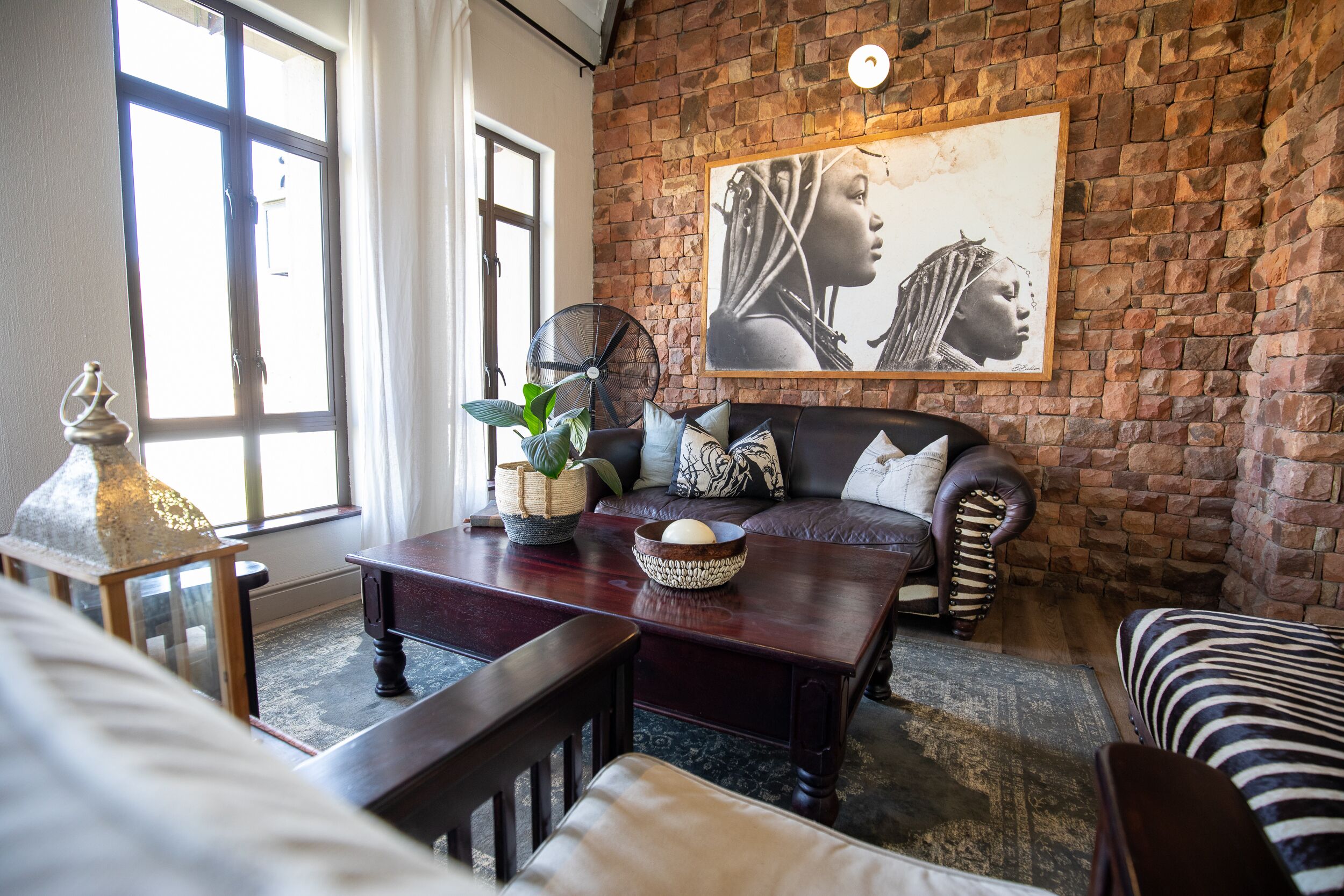 A cozy living room with a brick wall, a large window, a sofa, a coffee table, and a decorative bowl.