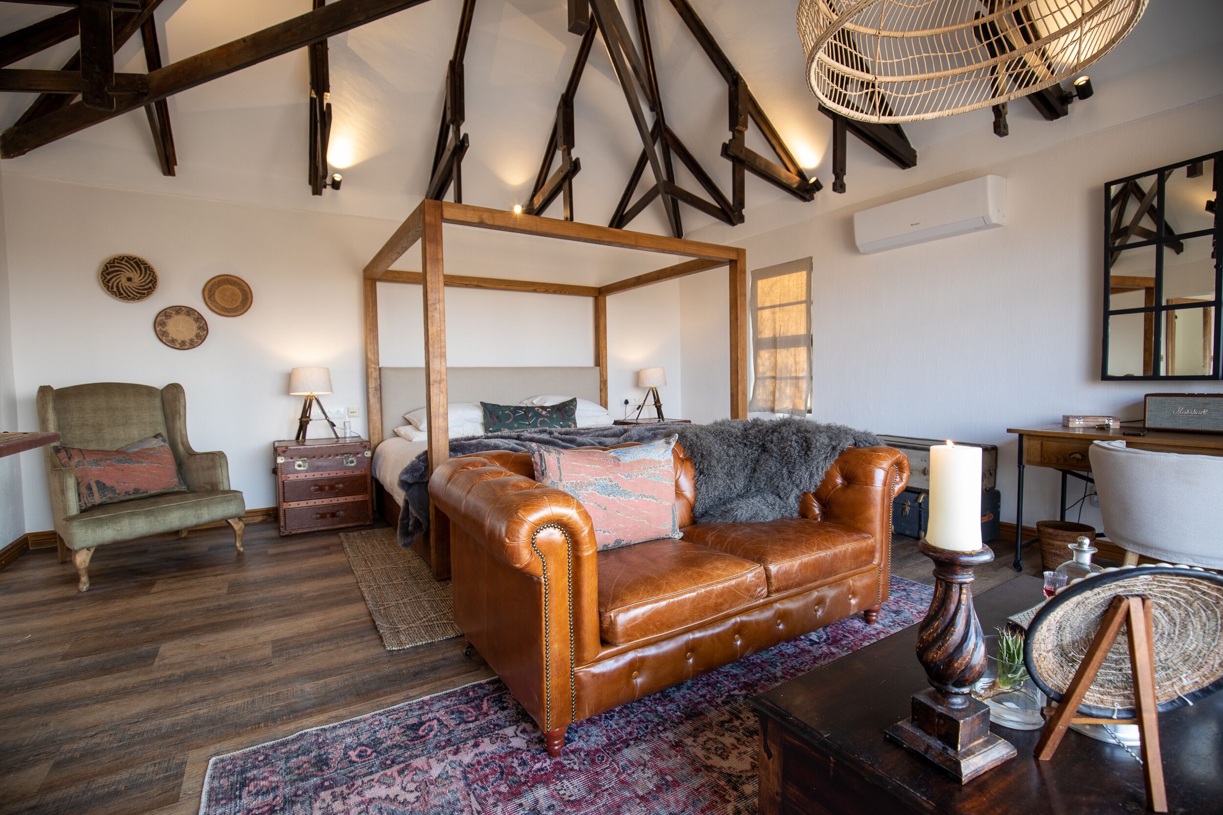 Une chambre à l’ancienne, dotée d’un lit à baldaquin, d’un canapé en cuir et d’un plafond en bois rustique.