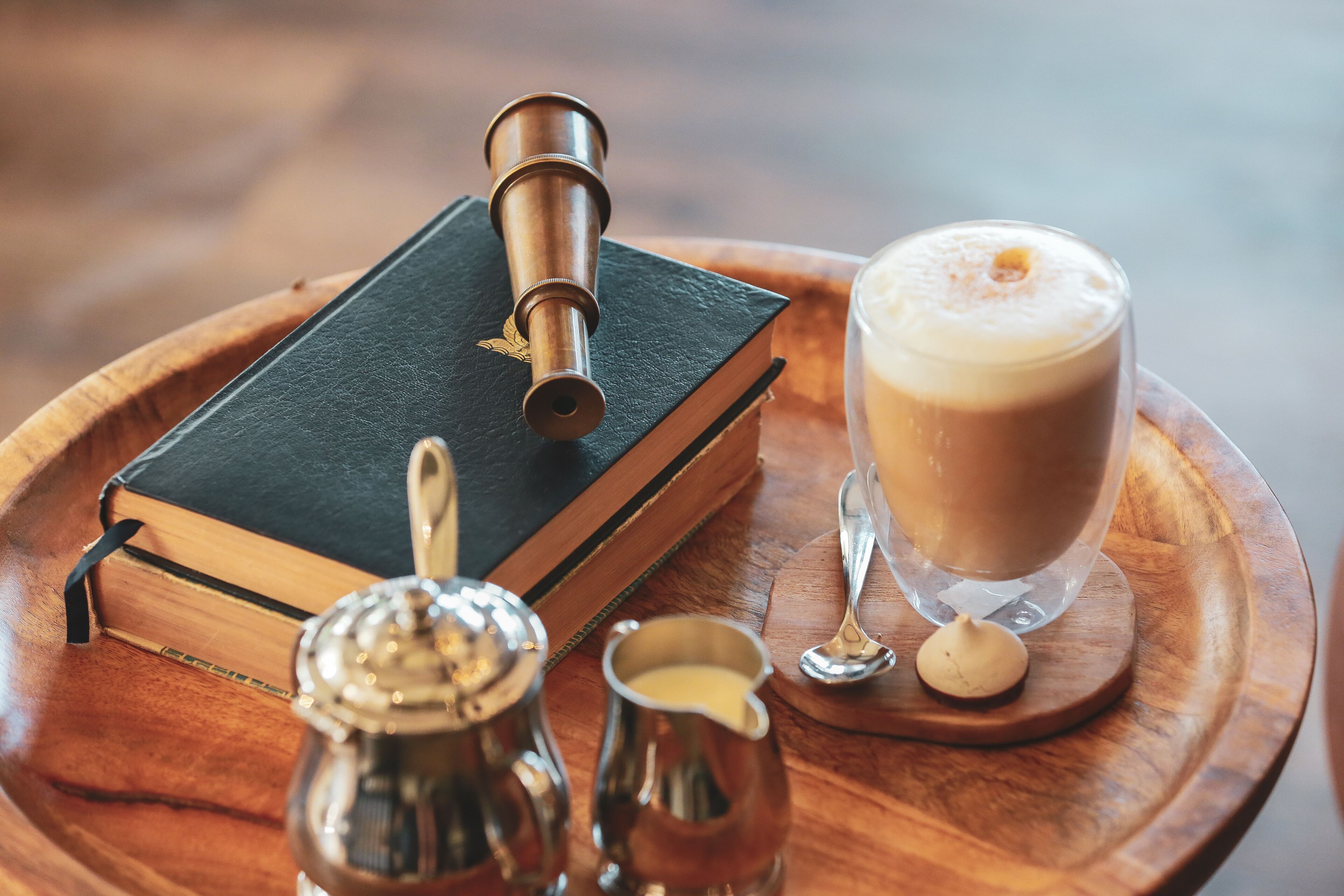 Una bandeja de madera con un libro, un telescopio, una taza de café y un azucarero.