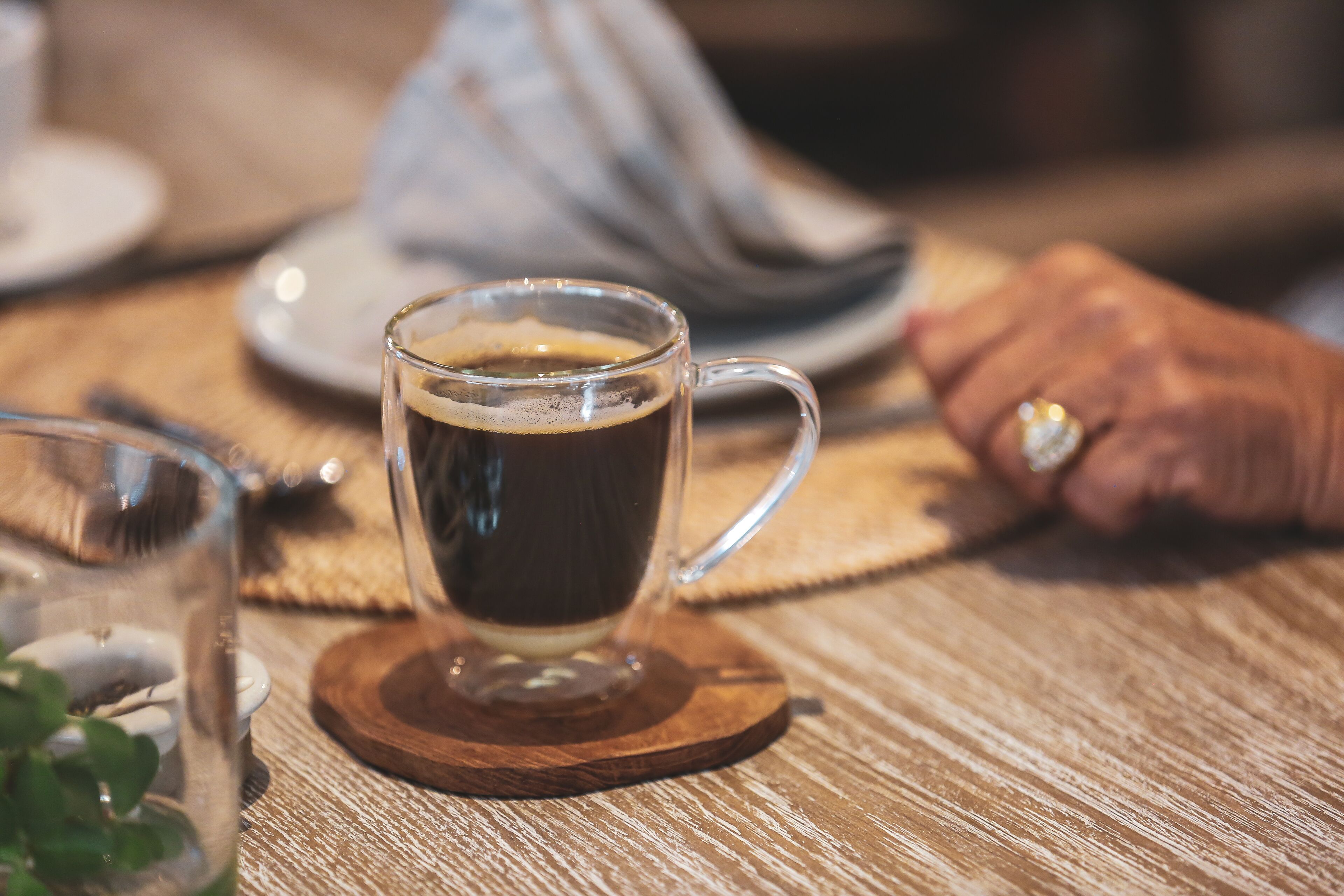 Eine transparente Kaffeetasse auf einem Holzteller.