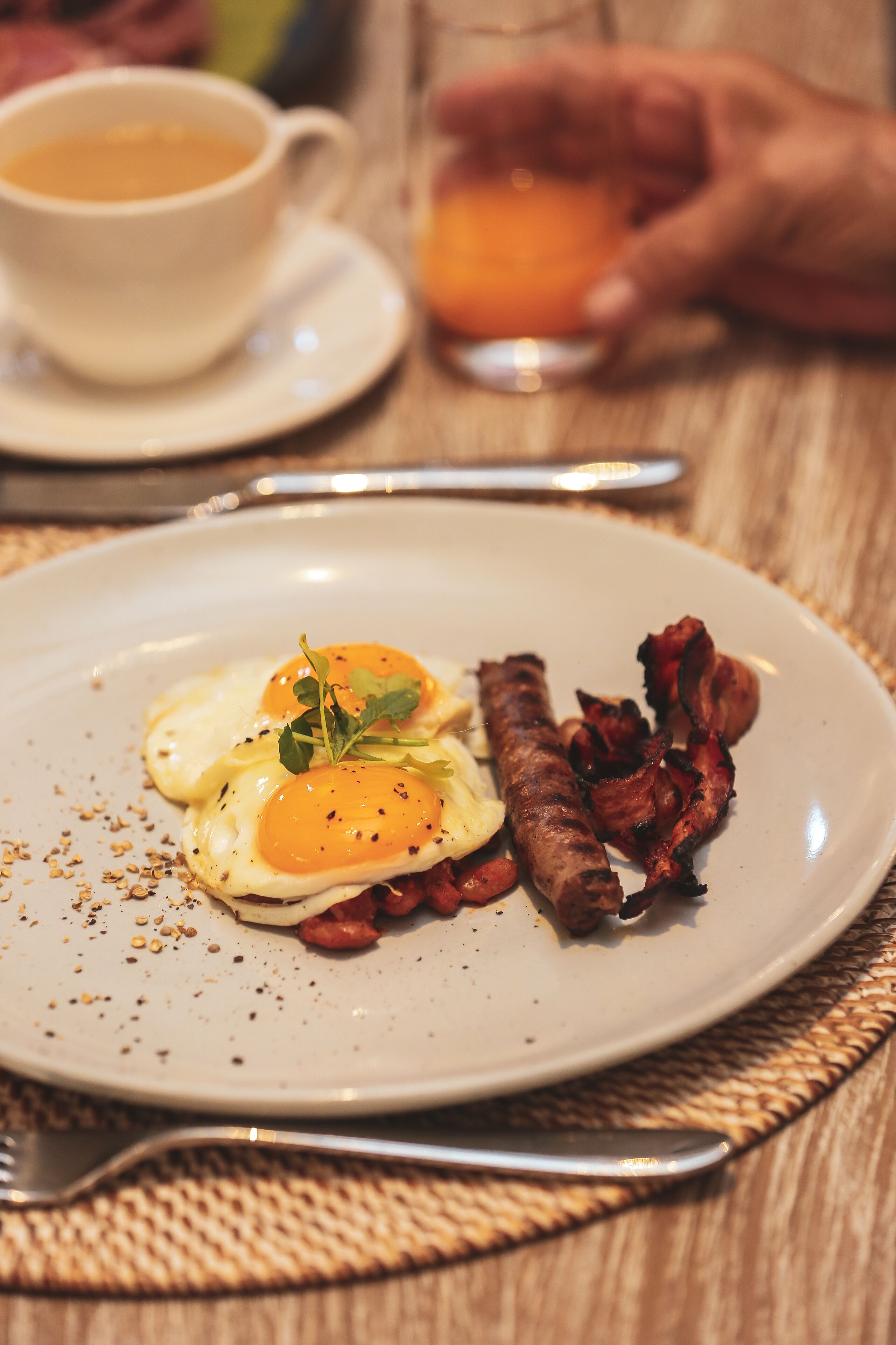 Une assiette avec des œufs, du bacon et une tasse de café, posée sur une table.