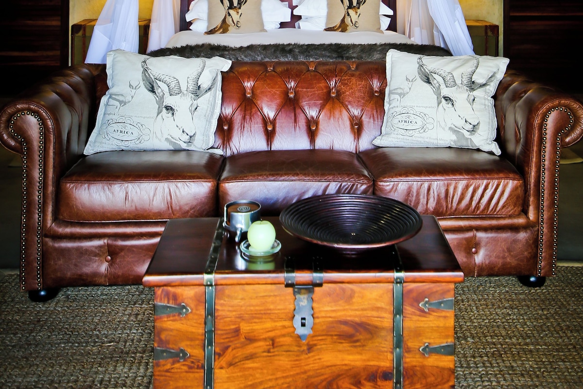 A bedroom with a canopy bed, leather sofa, and a wooden chest.