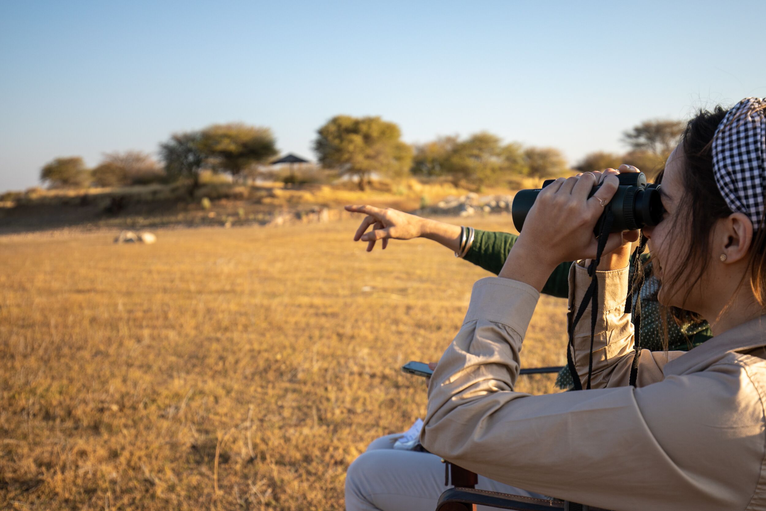 A person using binoculars in an open field with trees in the background.