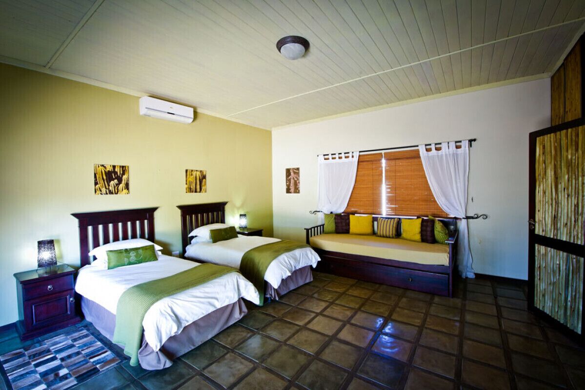 A bedroom with two beds, a window with curtains, a wooden wardrobe, and a tiled floor.