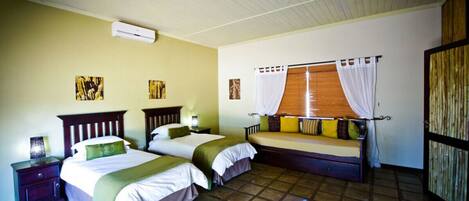 A bedroom with two beds, a window with curtains, a wooden wardrobe, and a tiled floor.