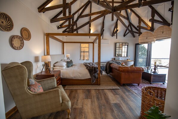 A spacious bedroom with a four-poster bed, a sitting area with a sofa and armchair, and a dining area with a table and chairs.