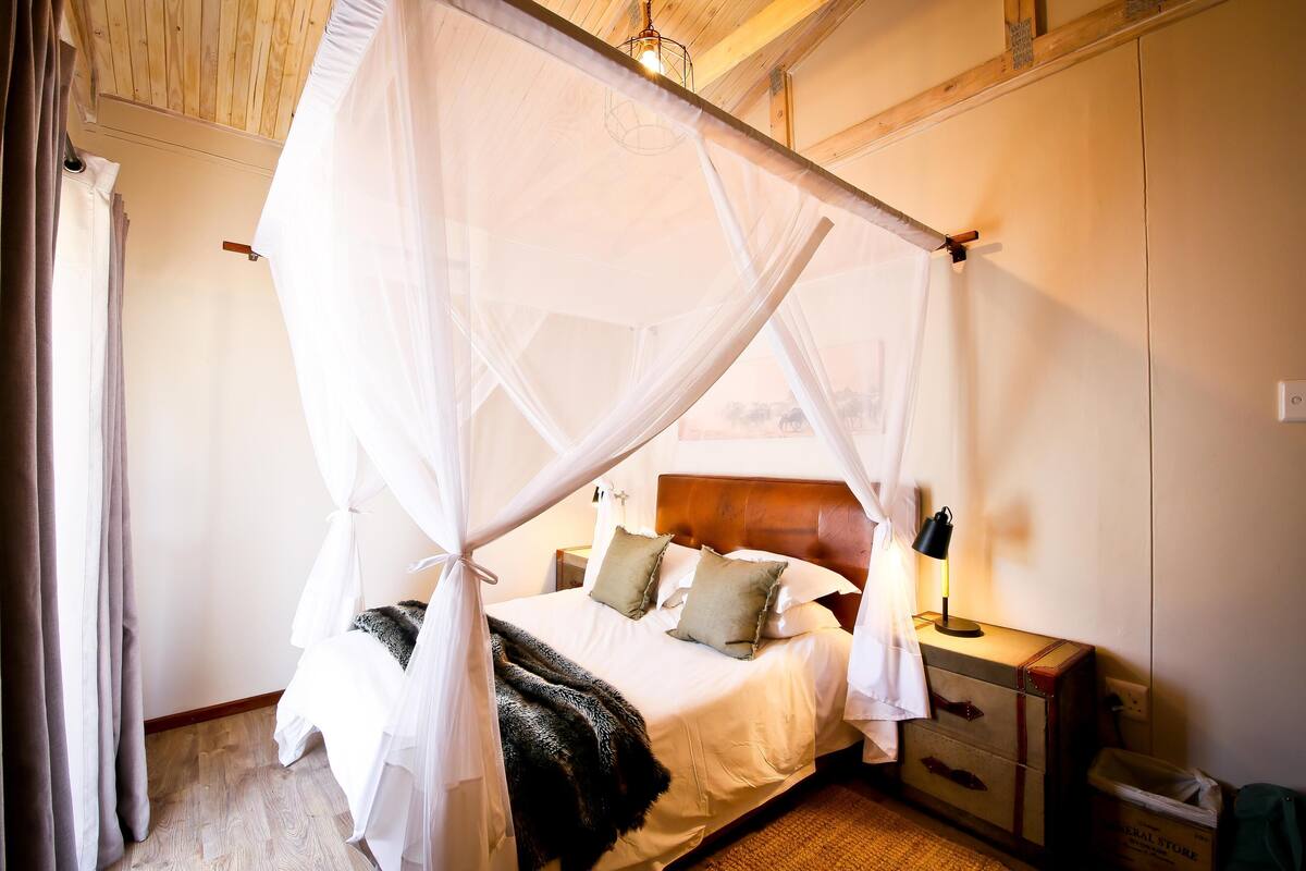 Une chambre à coucher avec un lit à baldaquin, une table de chevet, une lampe et une valise.