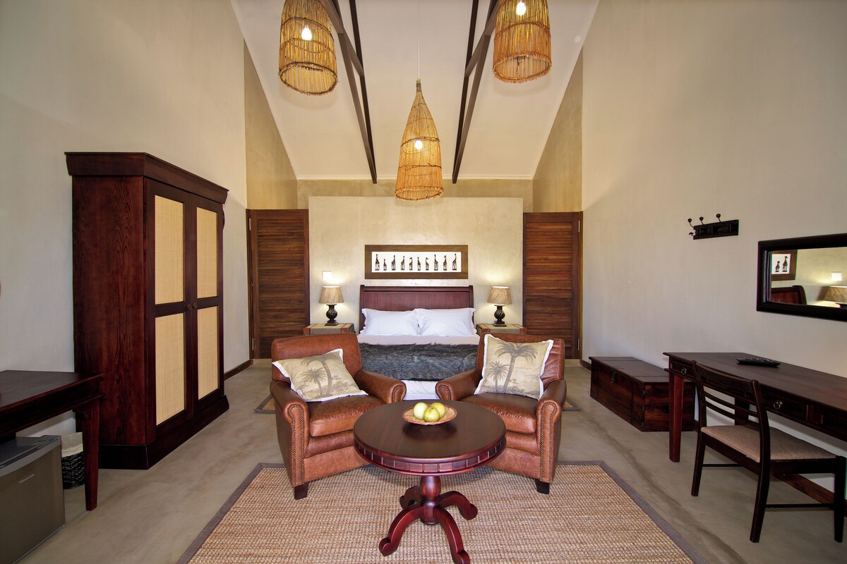 Une chambre à coucher comprenant un lit, deux fauteuils, une table ronde, un bureau et une armoire.