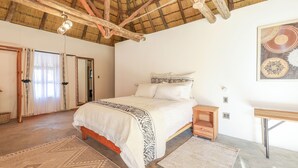 A bedroom with a bed, wooden nightstands, a desk, and a large mirror. - Ongula Village Homestead Lodge (Ondangwa)