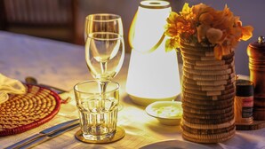 A table set for two with a candle, a vase of flowers, and a salt and pepper shaker. - Ongula Village Homestead Lodge (Ondangwa)