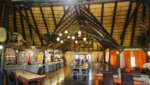 A spacious restaurant with high ceilings, wooden beams, and a thatched roof. Tables are set with chairs, and a bar is visible in the background. - Lapa Lange Game Lodge (Mariental)