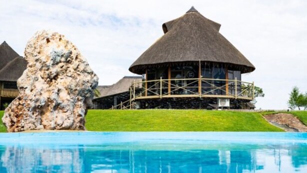 A resort with thatched-roof buildings, a swimming pool, and a large rock formation. - Lapa Lange Game Lodge (Mariental)