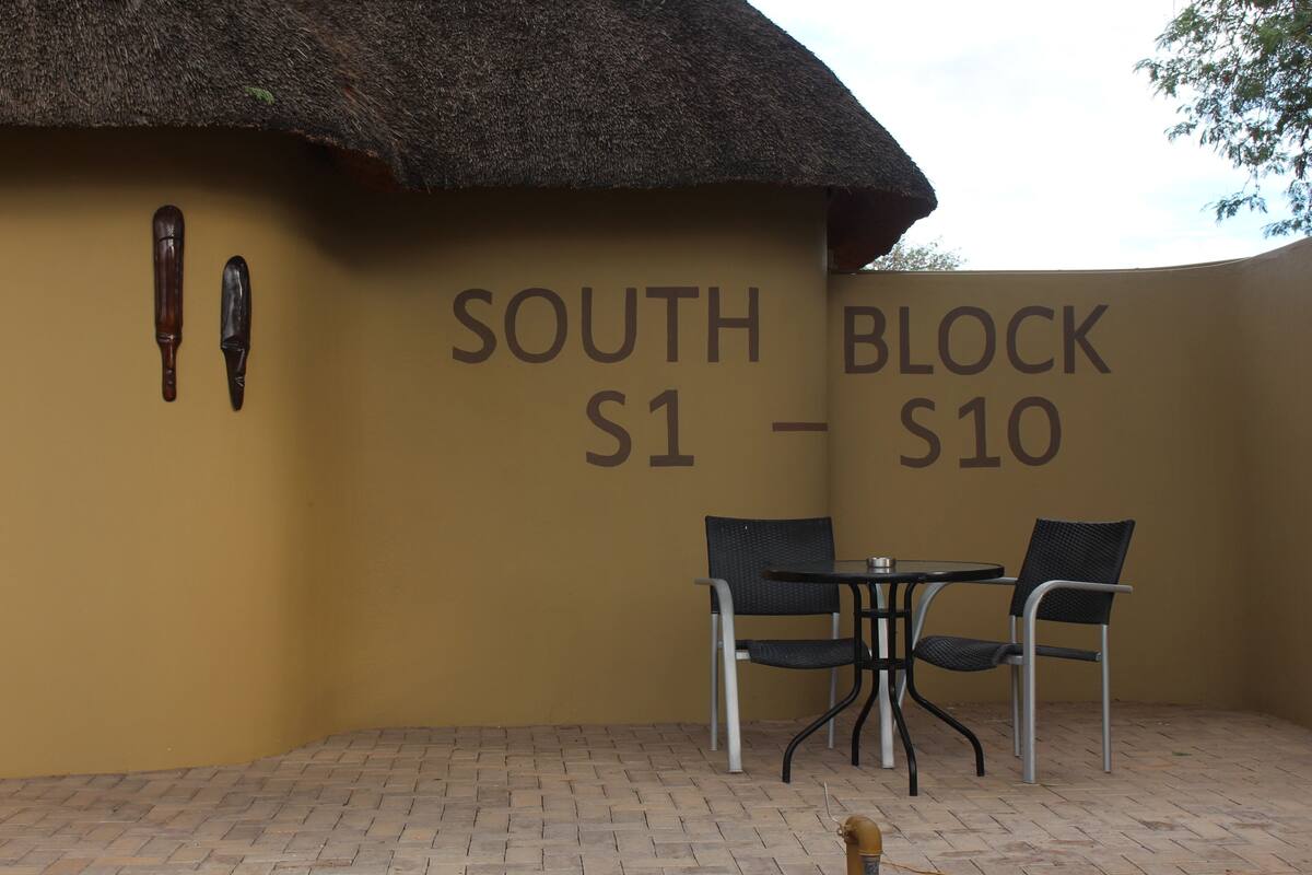 Ein Gebäude mit einem Schild, auf dem 'SOUTH BLOCK S1 - S10' steht, zwei Stühle und ein Tisch.