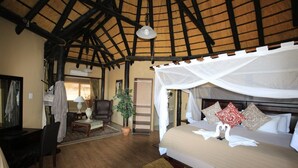 A spacious room with a high ceiling, a bed with a canopy, a desk, a chair, a lamp, and a potted plant. - Lapa Lange Game Lodge (Mariental)