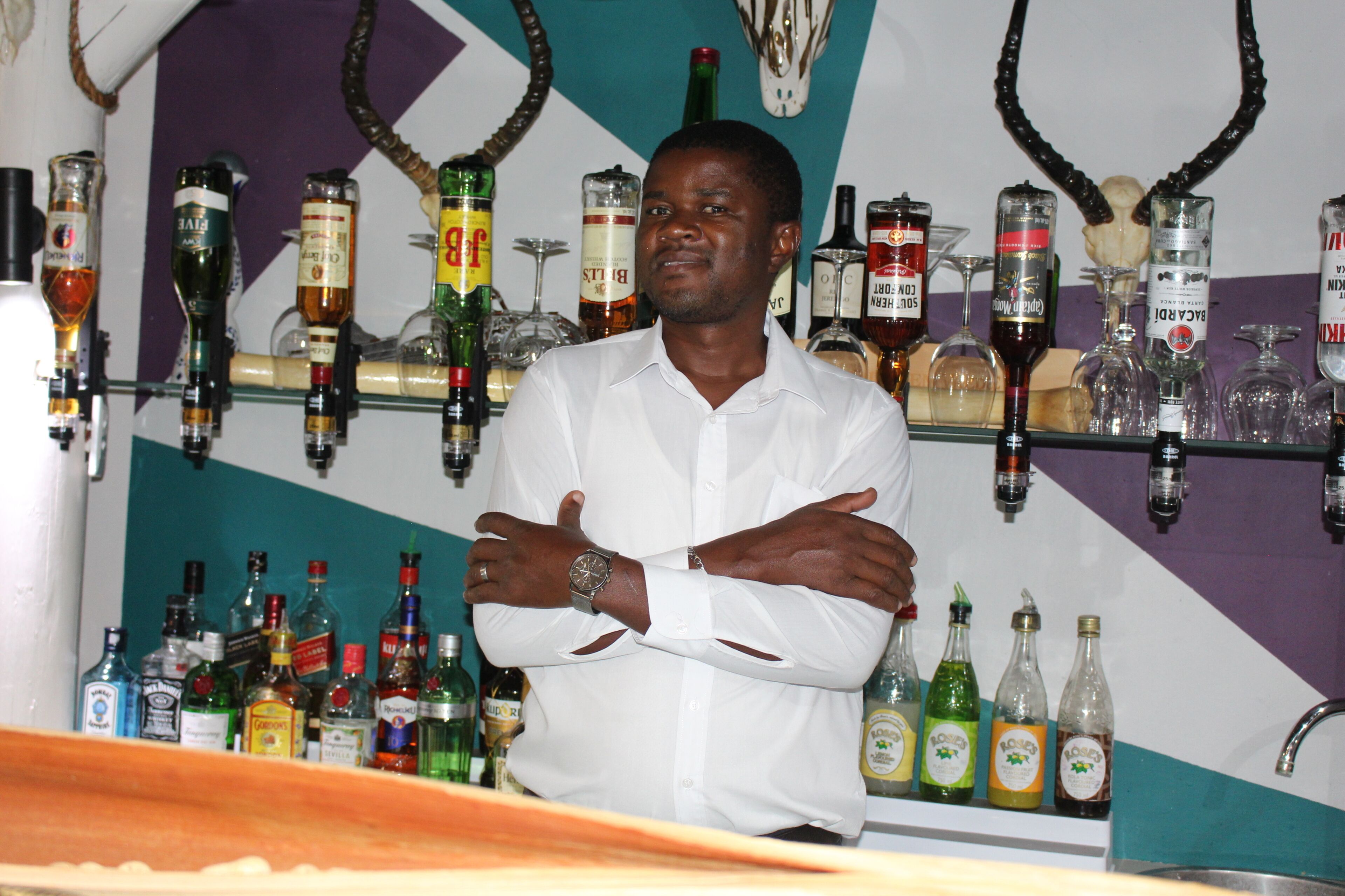 A man standing in front of a bar with various liquor bottles and glasses.