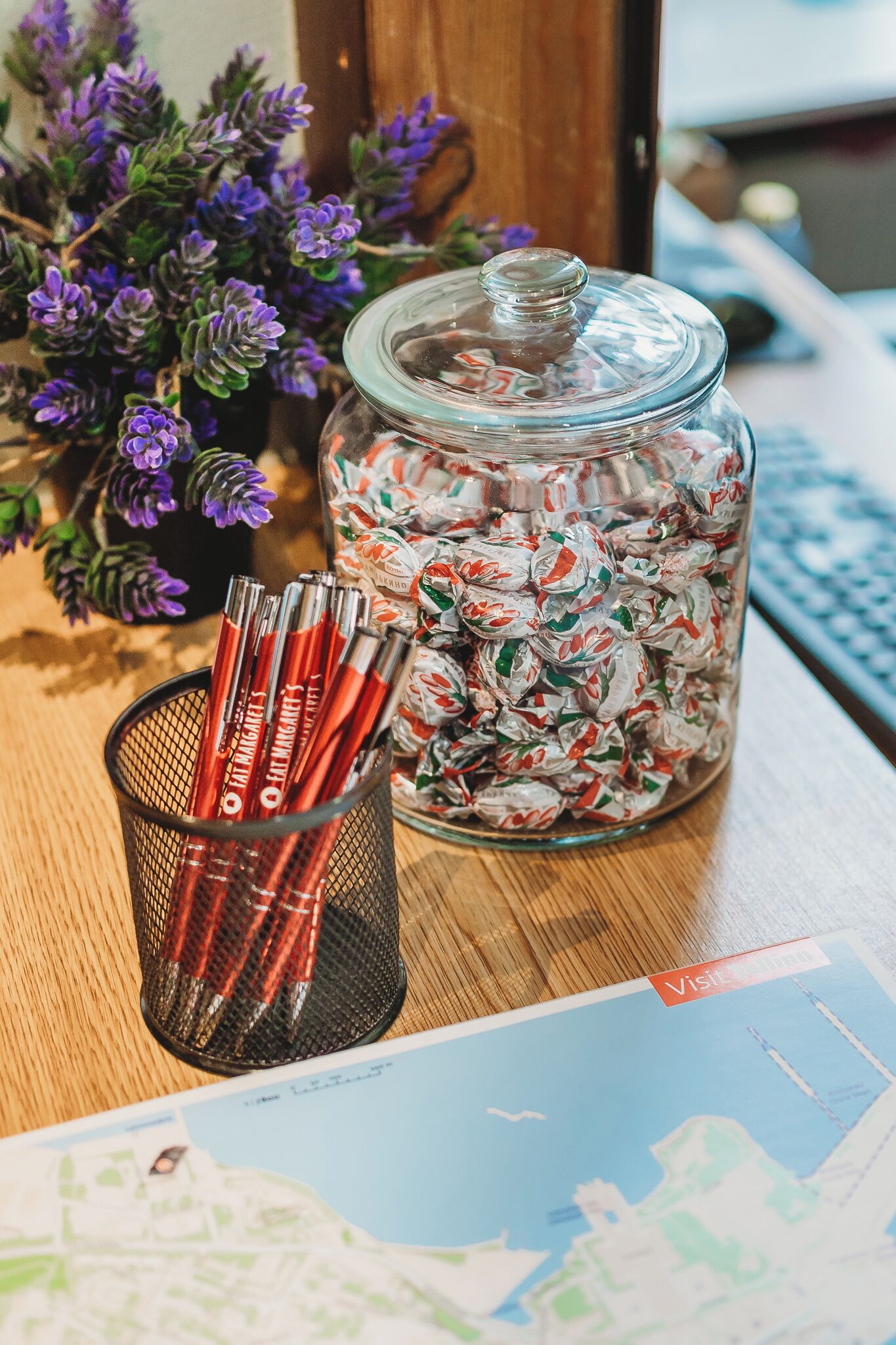 A desk with a glass jar filled with wrapped candies, a metal pen holder with pens, and a map.