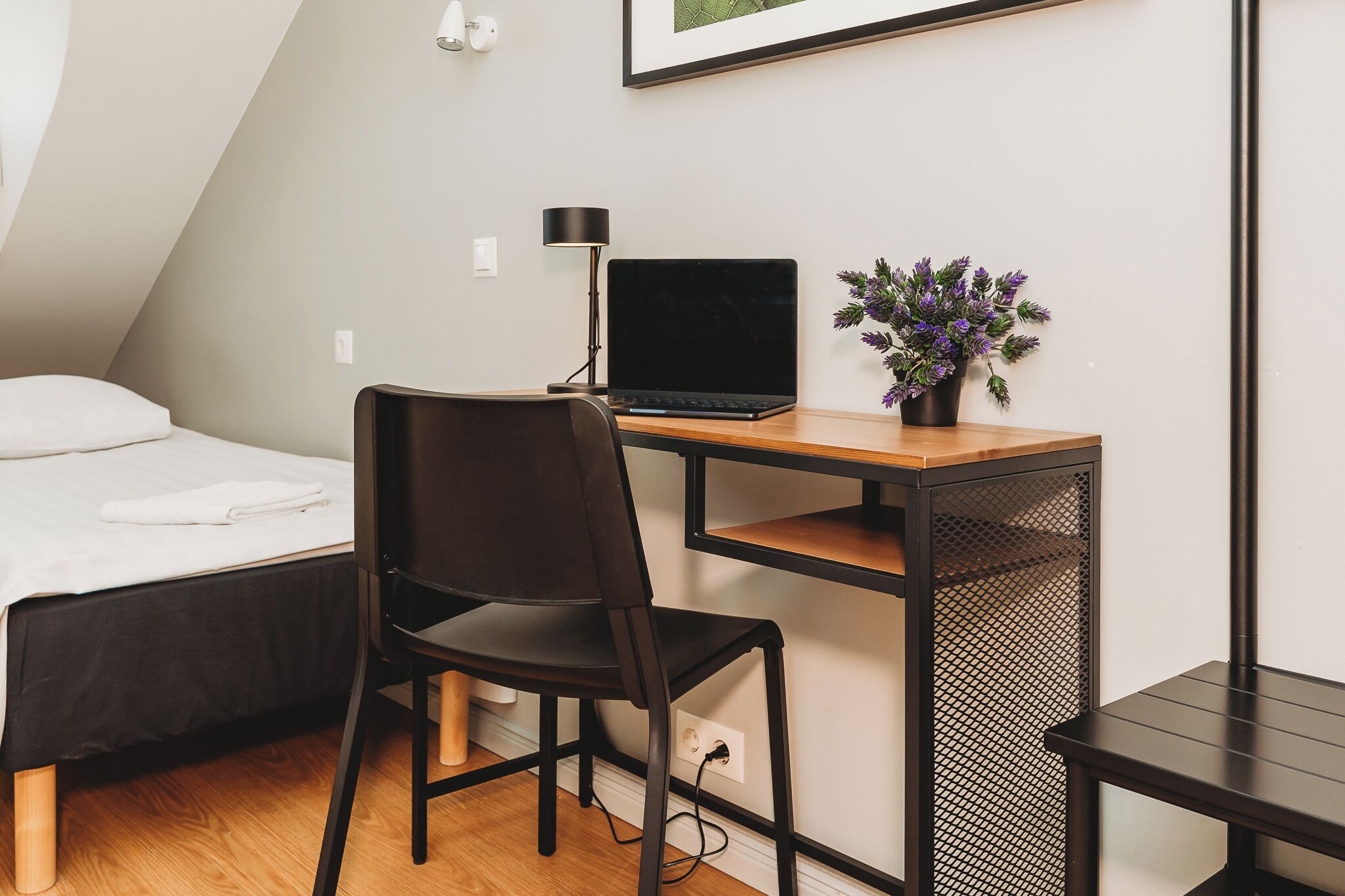A small, modern room with a bed, a desk with a laptop, a chair, and a potted plant.