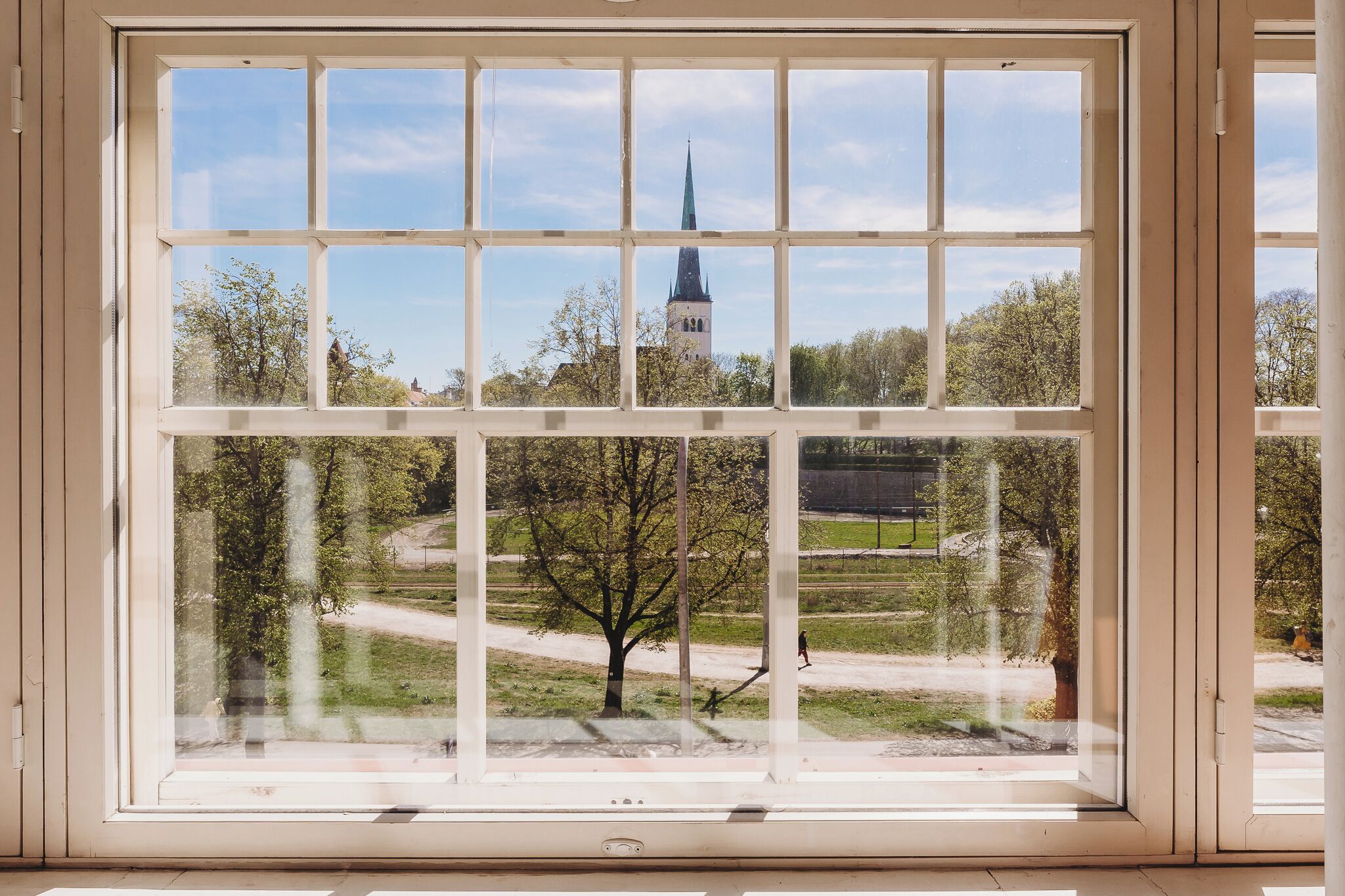 A window with a view of a church spire and a tree in the foreground.