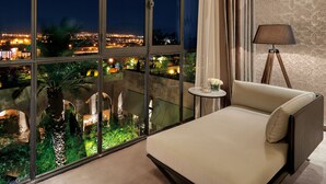 A bedroom with a large window, a bed, a nightstand, and a lamp.