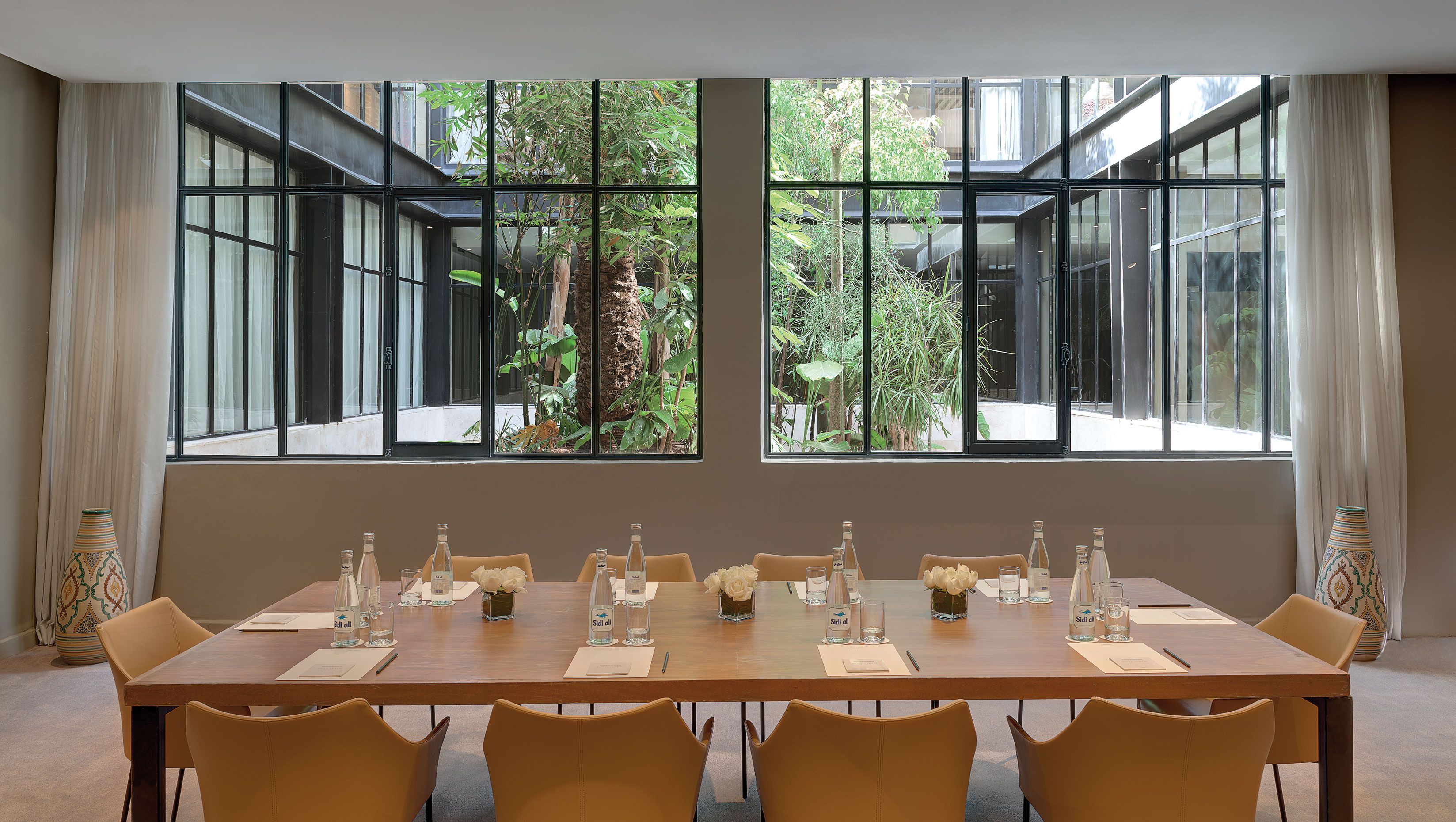 A conference room with a long table set for meetings, large windows with a view of greenery, and traditional decor.