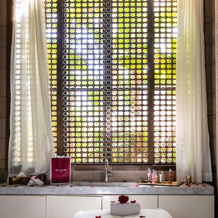 A room with a bed, a window with curtains, a sink, and toiletries on the counter.