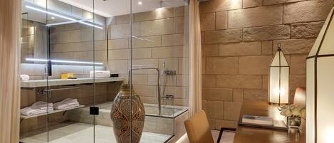 A modern bathroom with a glass shower enclosure, a large decorative vase, and a wooden vanity with a lamp.