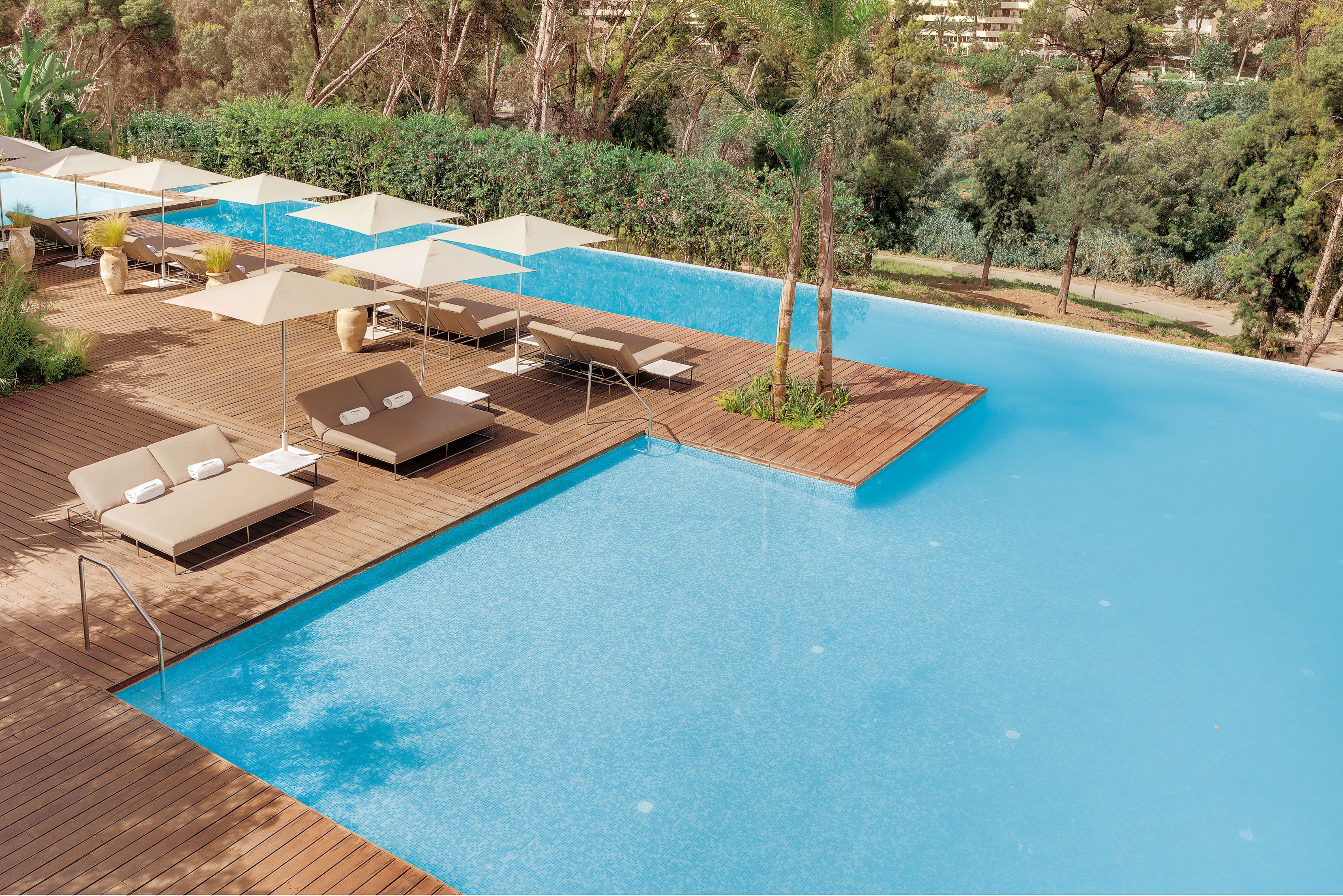 An outdoor swimming pool with wooden deck, lounge chairs, and umbrellas.