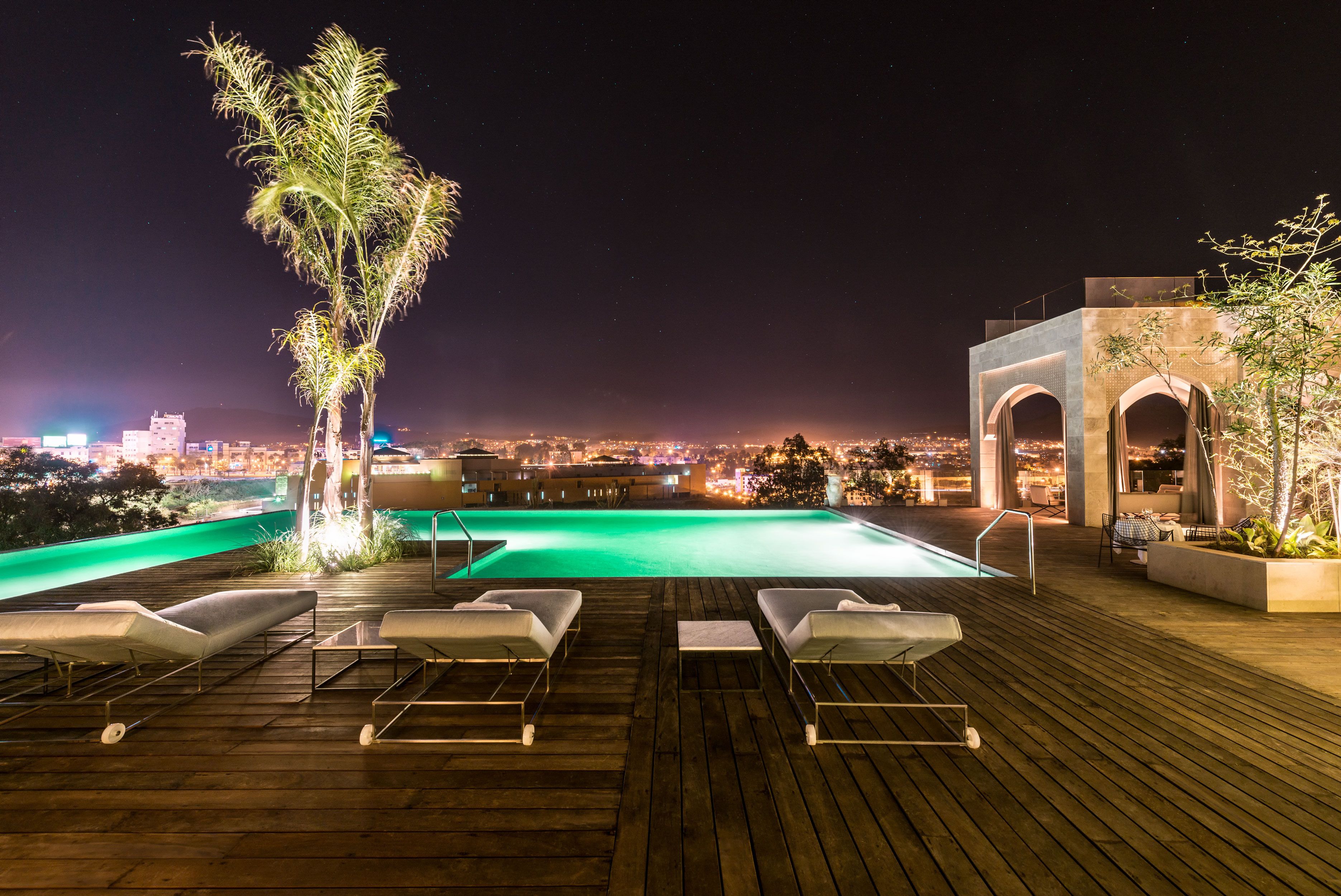 A rooftop pool area with lounge chairs and a view of the city at night.